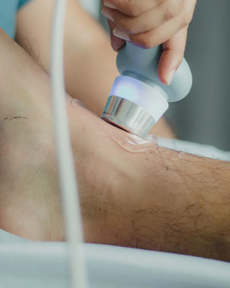 Aplicador de terapia por ondas encostado na pele da perna, com gel