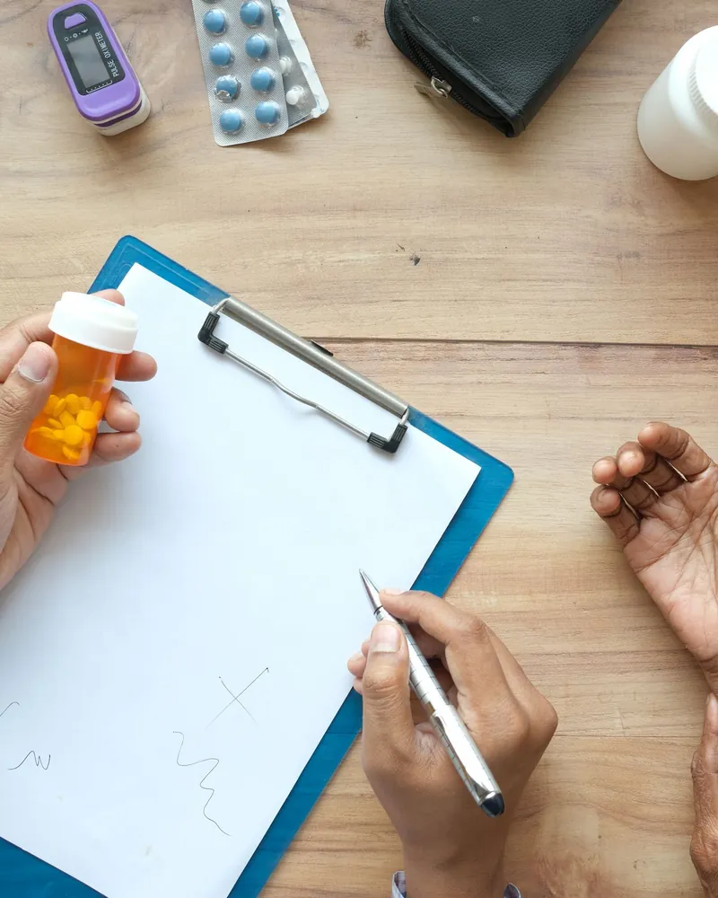 Consulta vista de cima: prancheta sobre a mesa e um frasco de remédio na mão do médico